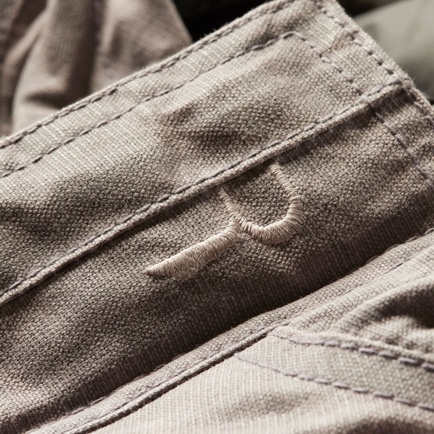 Close-up of a brown jacket with a brand logo on the chest pocket.